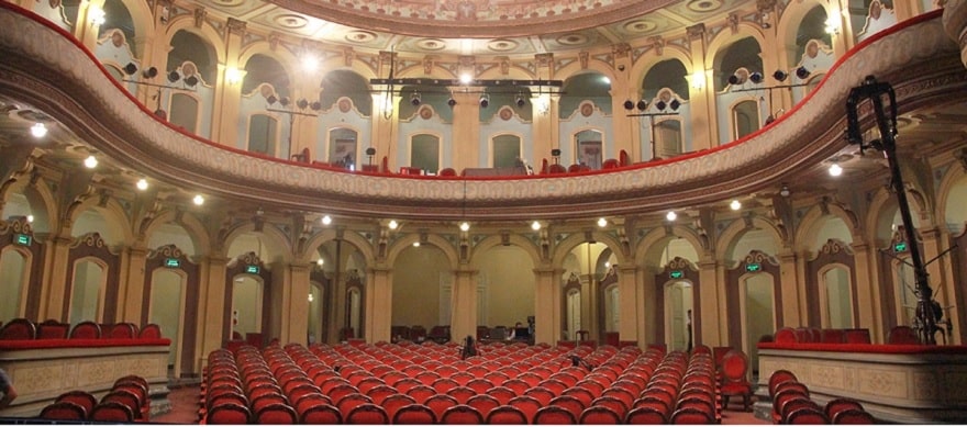 The auditorium features an open circular-arc layout, with the open section seamlessly connecting to the stage via the proscenium arch. The seating area consists of approximately 350 wooden chairs upholstered in rich red wool.